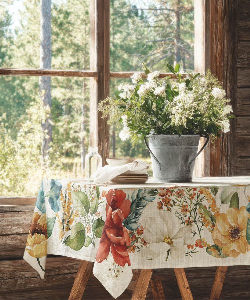 Elegante tovaglia floreale antimacchia modello Blossom stesa su una tavola in una luminosa sala da pranzo. Un complemento d'arredo pratico e accogliente in polylino effetto lino.