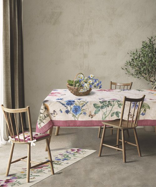 Tovaglia antimacchia modello Erbacee stesa su un tavolo da pranzo rettangolare in legno chiaro, all'interno di una sala da pranzo moderna e luminosa.