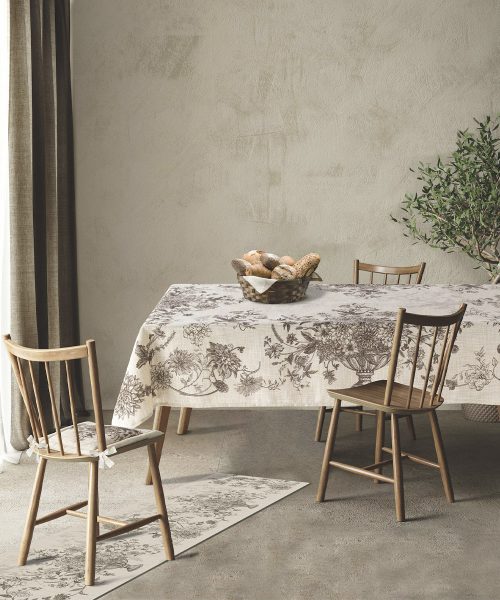 Tovaglia antimacchia modello Toile stesa su un tavolo da pranzo in legno, in una stanza elegante con sedie coordinate, un cesto di pane al centro e passatoia abbinata a terra.