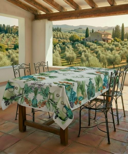 Tavolo in veranda con Tovaglia in cotone con stampa digitale e Prodotta in Italia. Disegno erbbe aromatiche e olive su fondo chiaro effetto lino. Due misure per tavoli da 6 e da 12 persone.